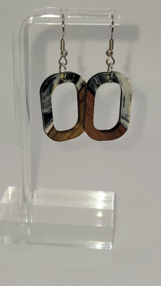 O shaped earrings made of wooden and epoxy earring a walnut colored wood. Colored with a black, white sparkle epoxy. Displayed on a clear stand against a white background