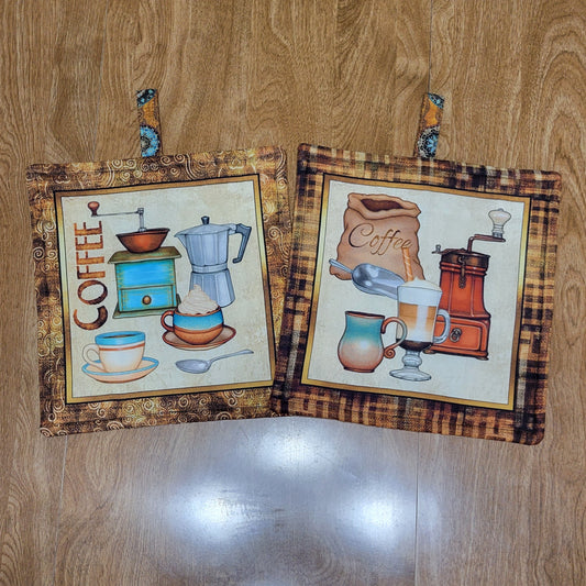 Two coffee-themed pot holders with a brown, black, and golden border on a wood surface
