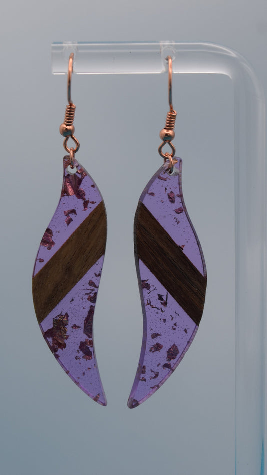The earring is a translucent purple resin. This resin has a smooth, polished finish, allowing some light to pass through, giving it a luminous quality. Embedded within the resin are numerous small, irregular rose gold flakes with a walnut color piece of wood set in the middle of the earring. These flakes are scattered randomly, catching the light and adding a subtle, delicate shimmer and texture to the surface.