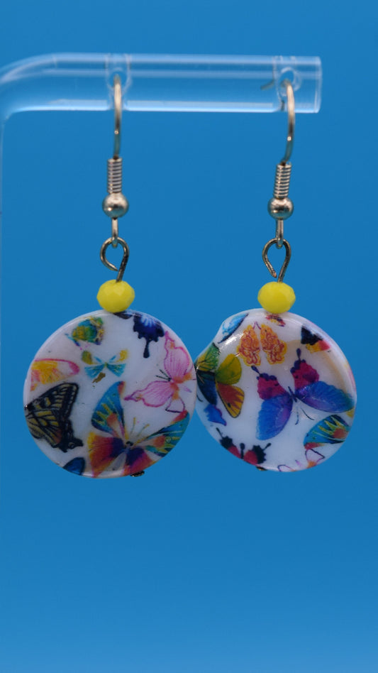 Colorful butterfly-patterned earrings Displayed on a clear stand against a teal background.