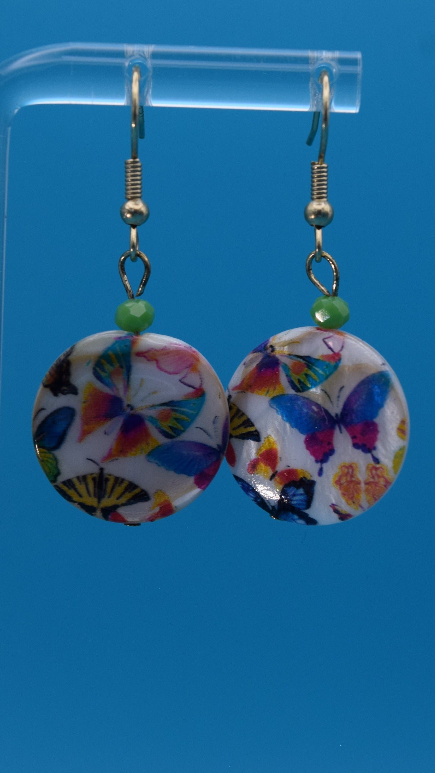 Colorful butterfly-patterned earrings Displayed on a clear stand against a teal background.