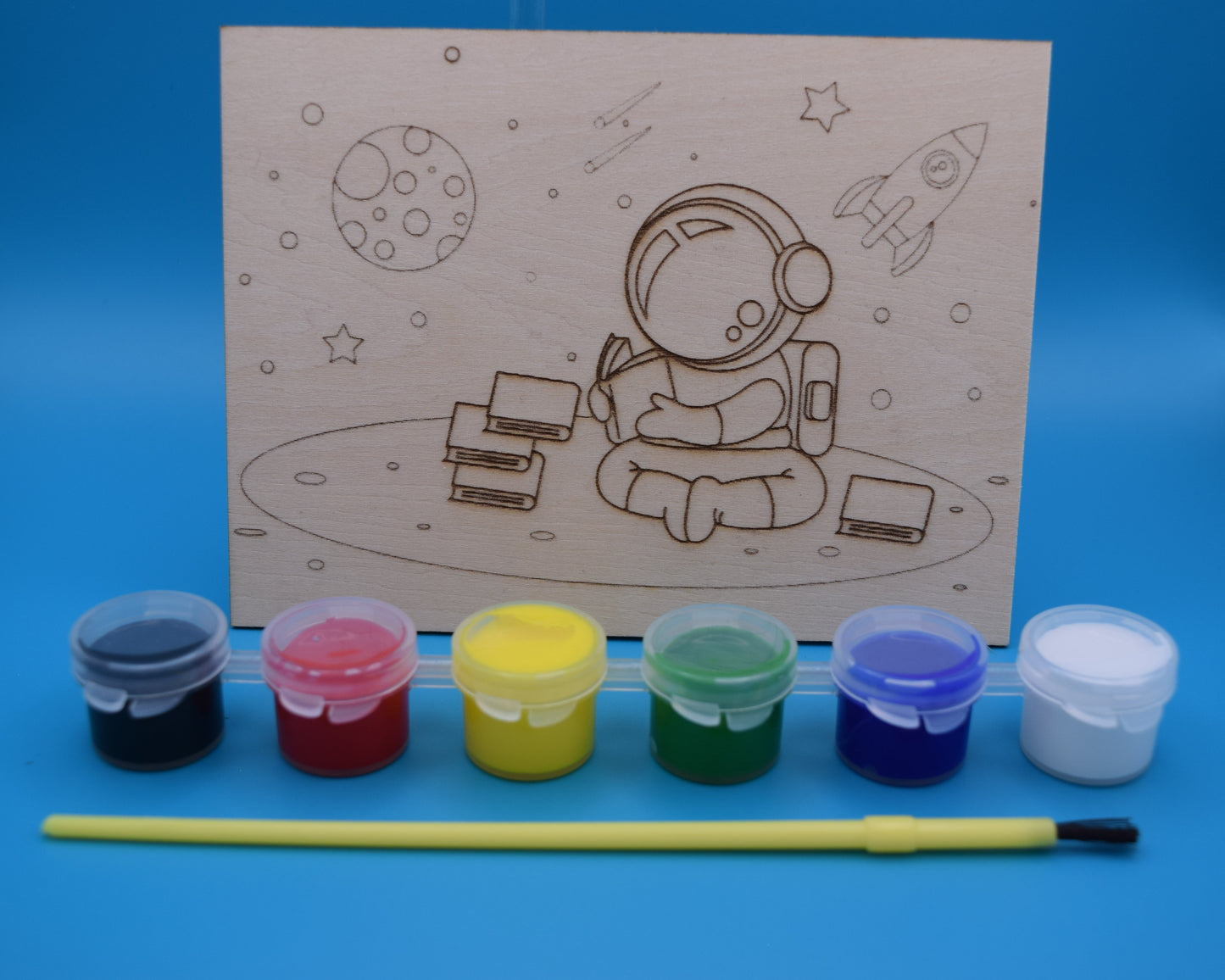 Children's craft kit with astronaut design on 3mm piece of wood, along with paints (black, red, yellow, green, blue and white are provided with a kids paint brush.