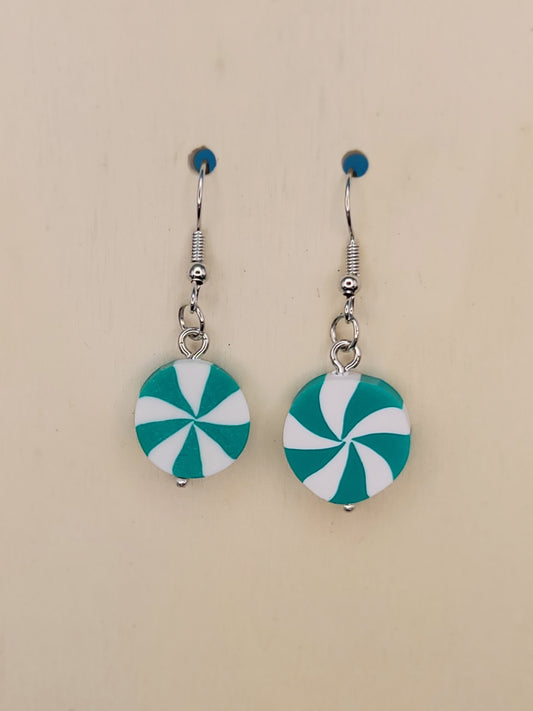 Pair of silicone green and white peppermint candy dangle earrings. That are 4 cm long with silver hooks and a tiny silver ball on the bottom. Displayed on a beige background.