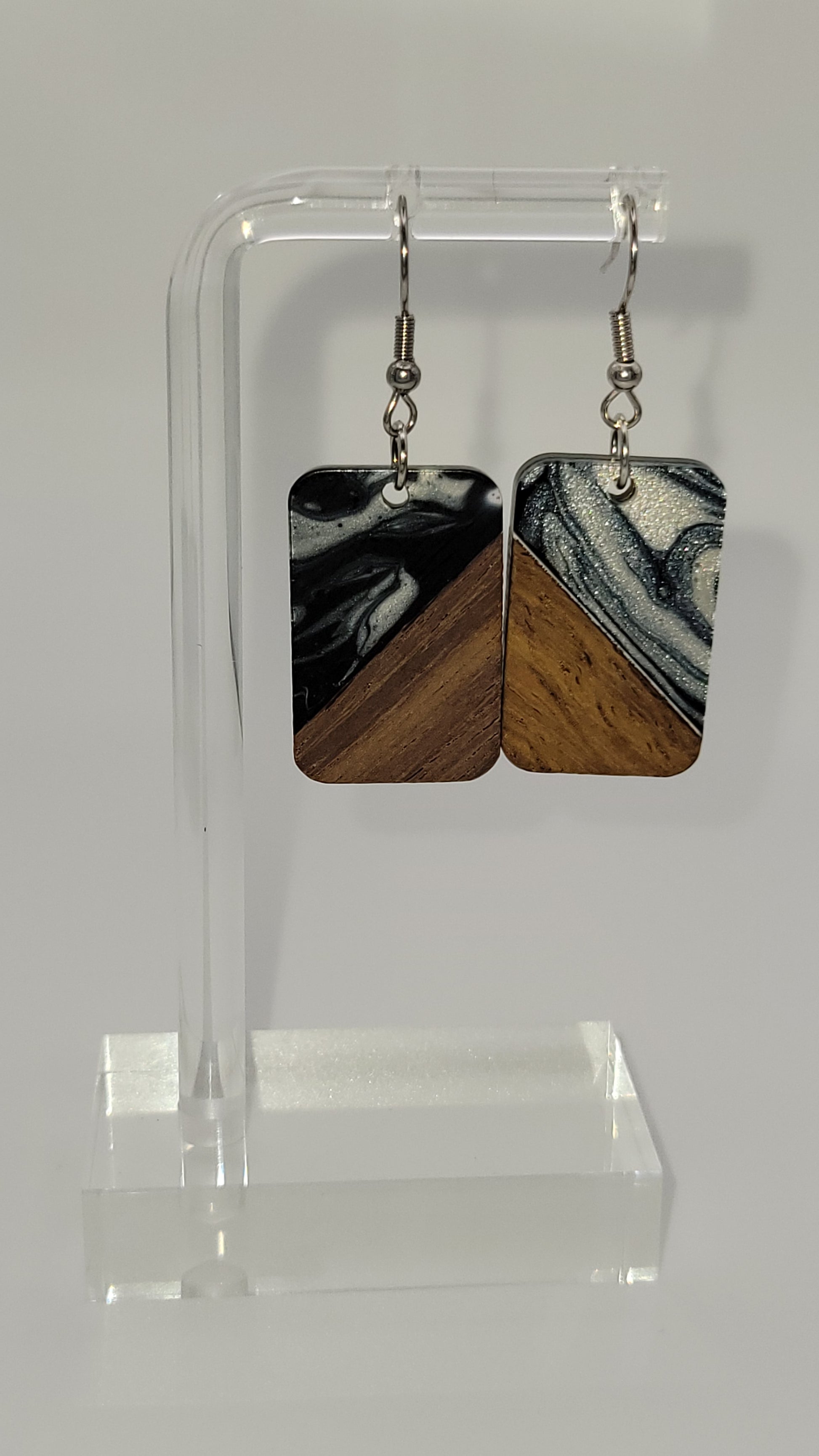 Rectangle shaped earrings made of wooden and epoxy earring a walnut colored wood.  Colored with a black, white sparkle epoxy. Displayed on a clear stand against a white background
