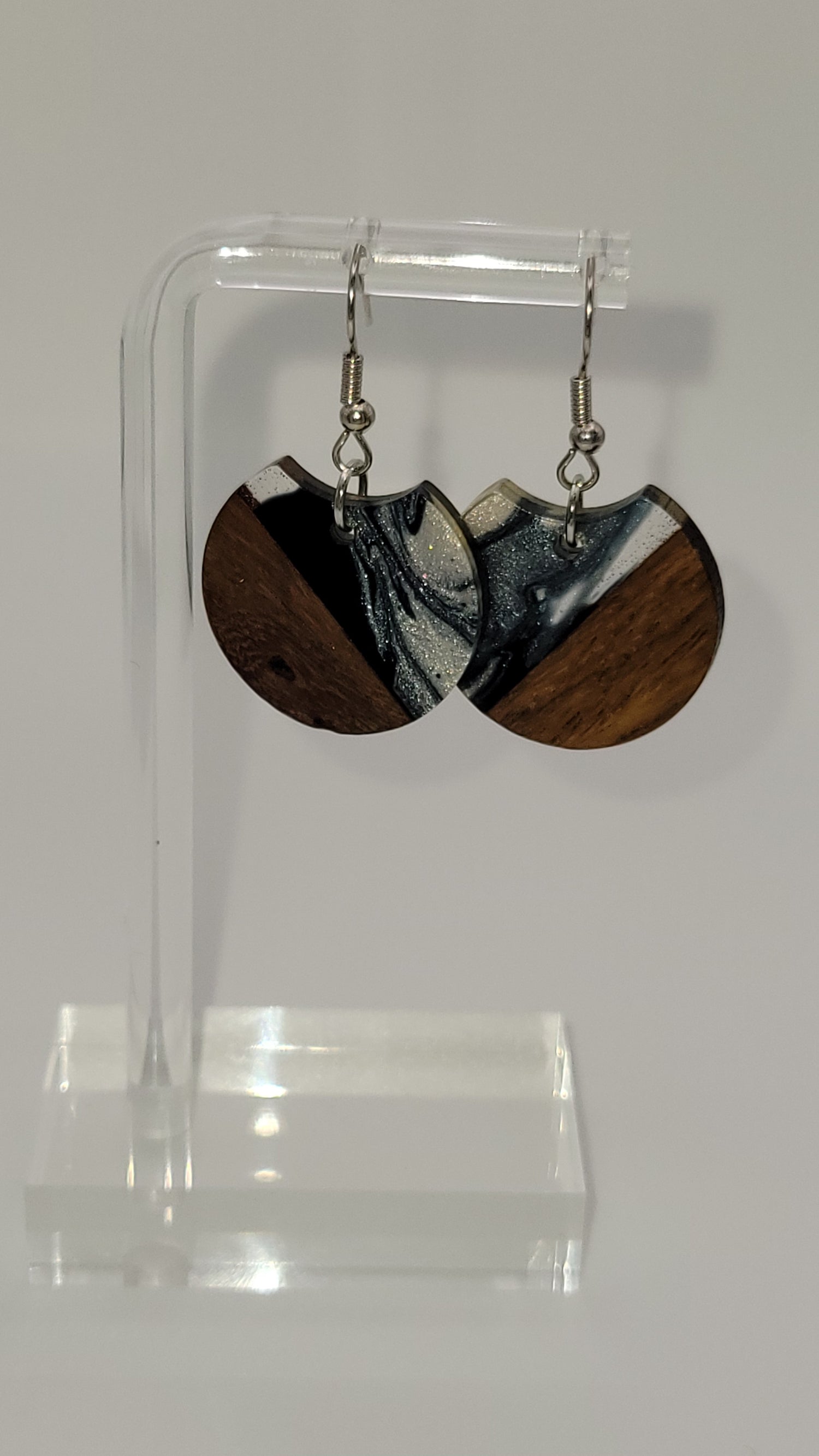 Segment of a circle earrings made of wooden and epoxy earring a walnut colored wood.  Colored with a black, white sparkle epoxy. Displayed on a clear stand against a white background