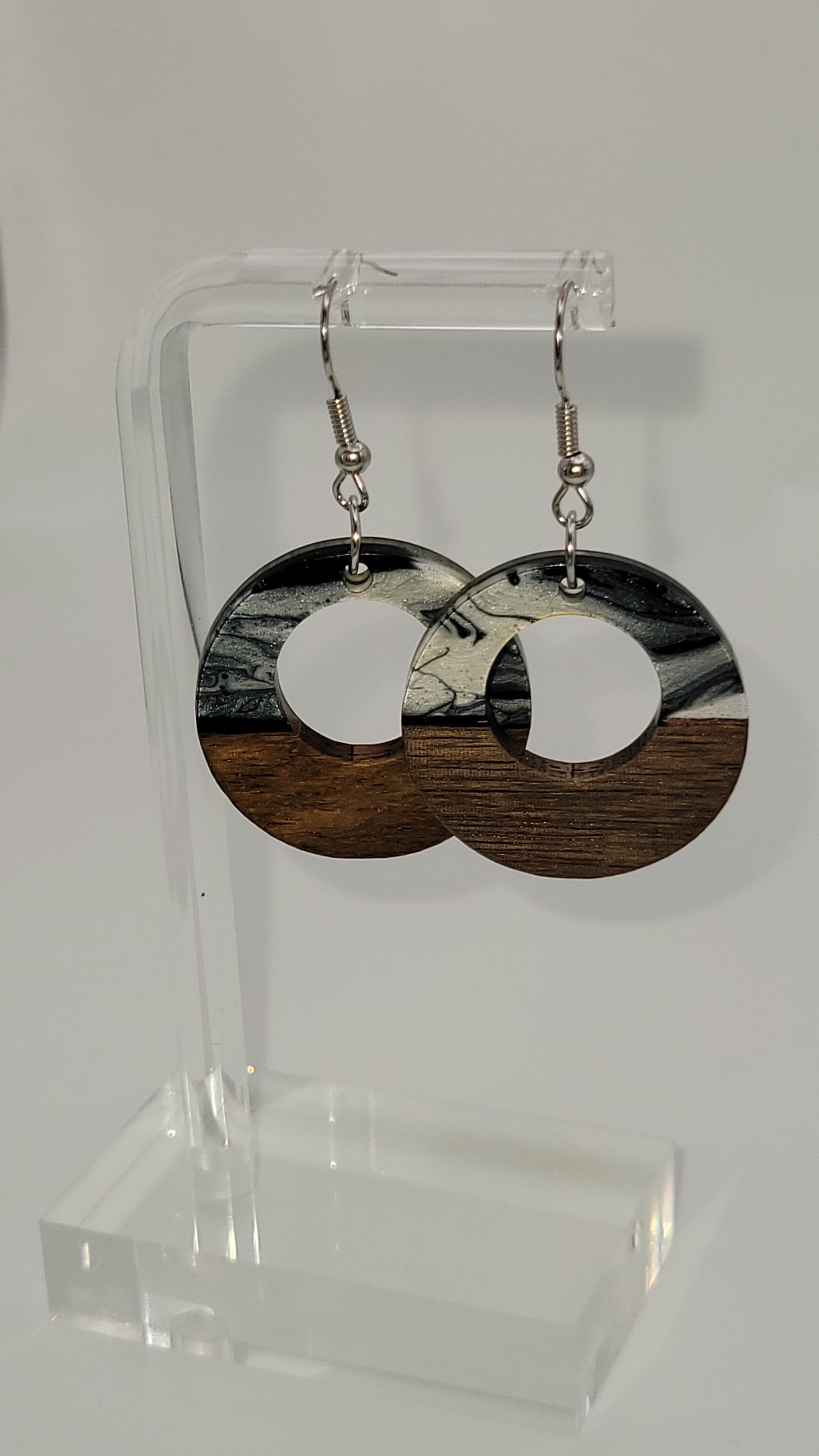 Donut shaped earrings made of wooden and epoxy earring a walnut colored wood.  Colored with a black, white sparkle epoxy. Displayed on a clear stand against a white background