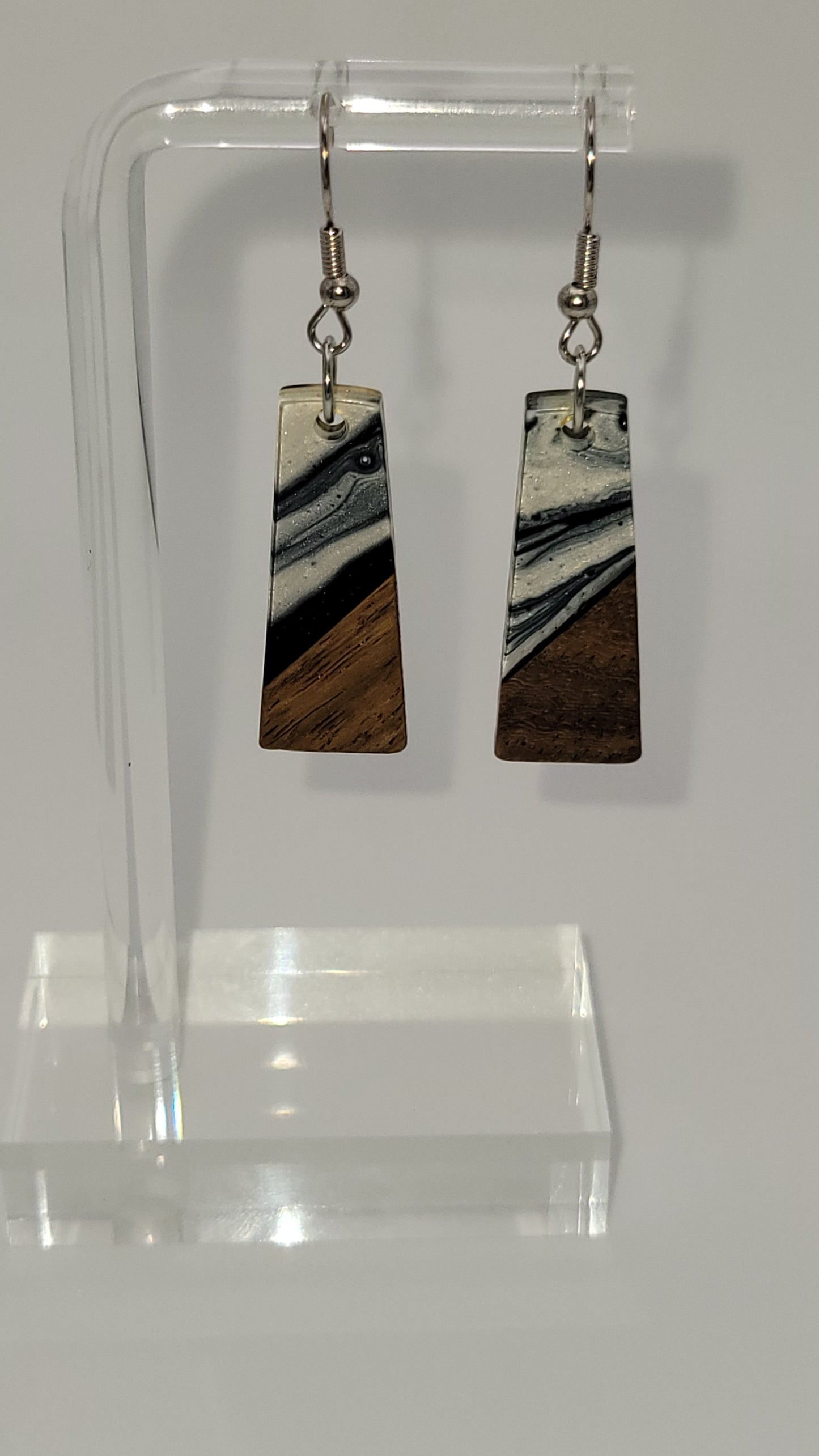  Elongated rectangles earrings made of wooden and epoxy earring a walnut colored wood.  Colored with a black, white sparkle epoxy. Displayed on a clear stand against a white background