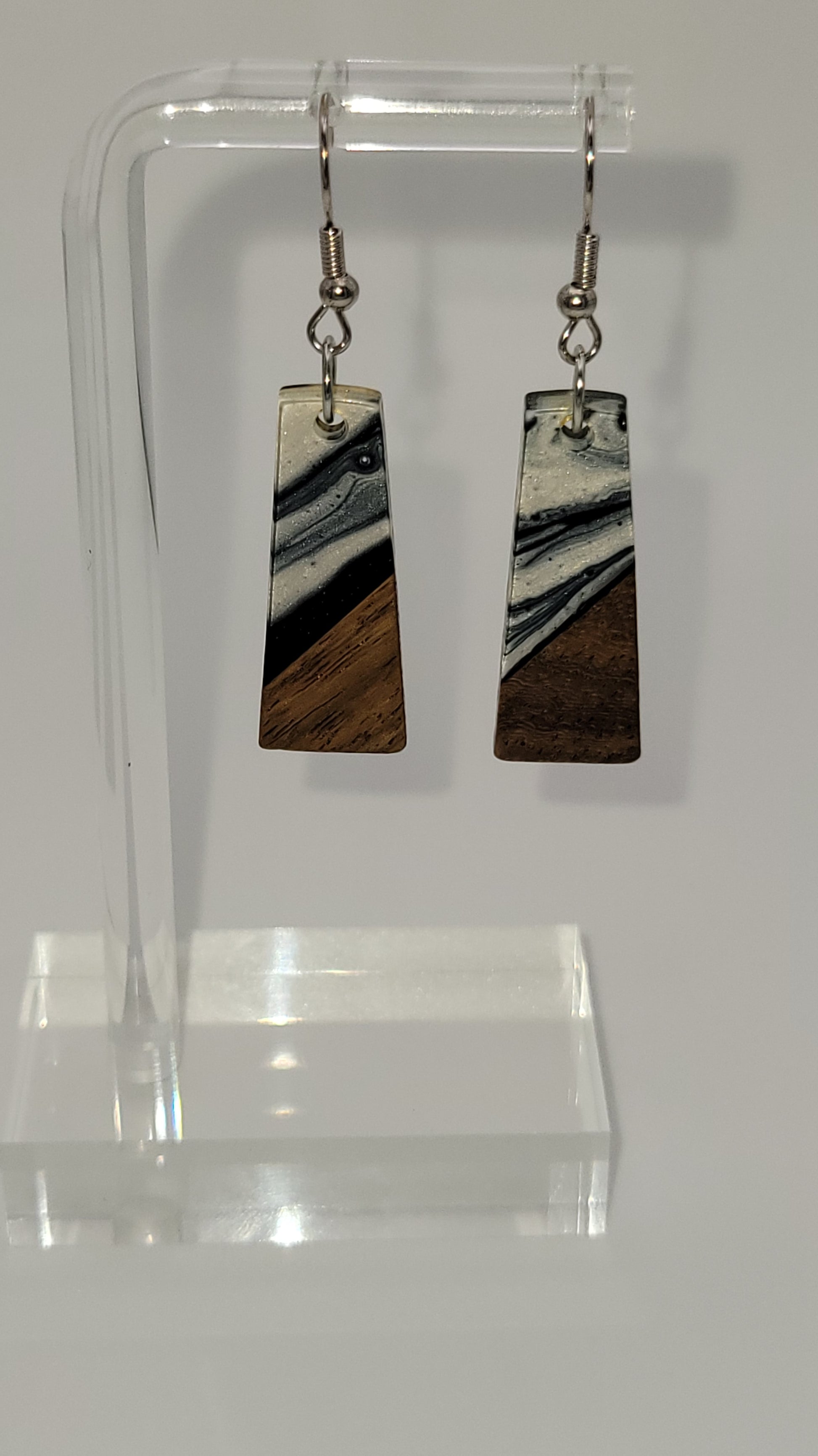  Elongated rectangles earrings made of wooden and epoxy earring a walnut colored wood.  Colored with a black, white sparkle epoxy. Displayed on a clear stand against a white background