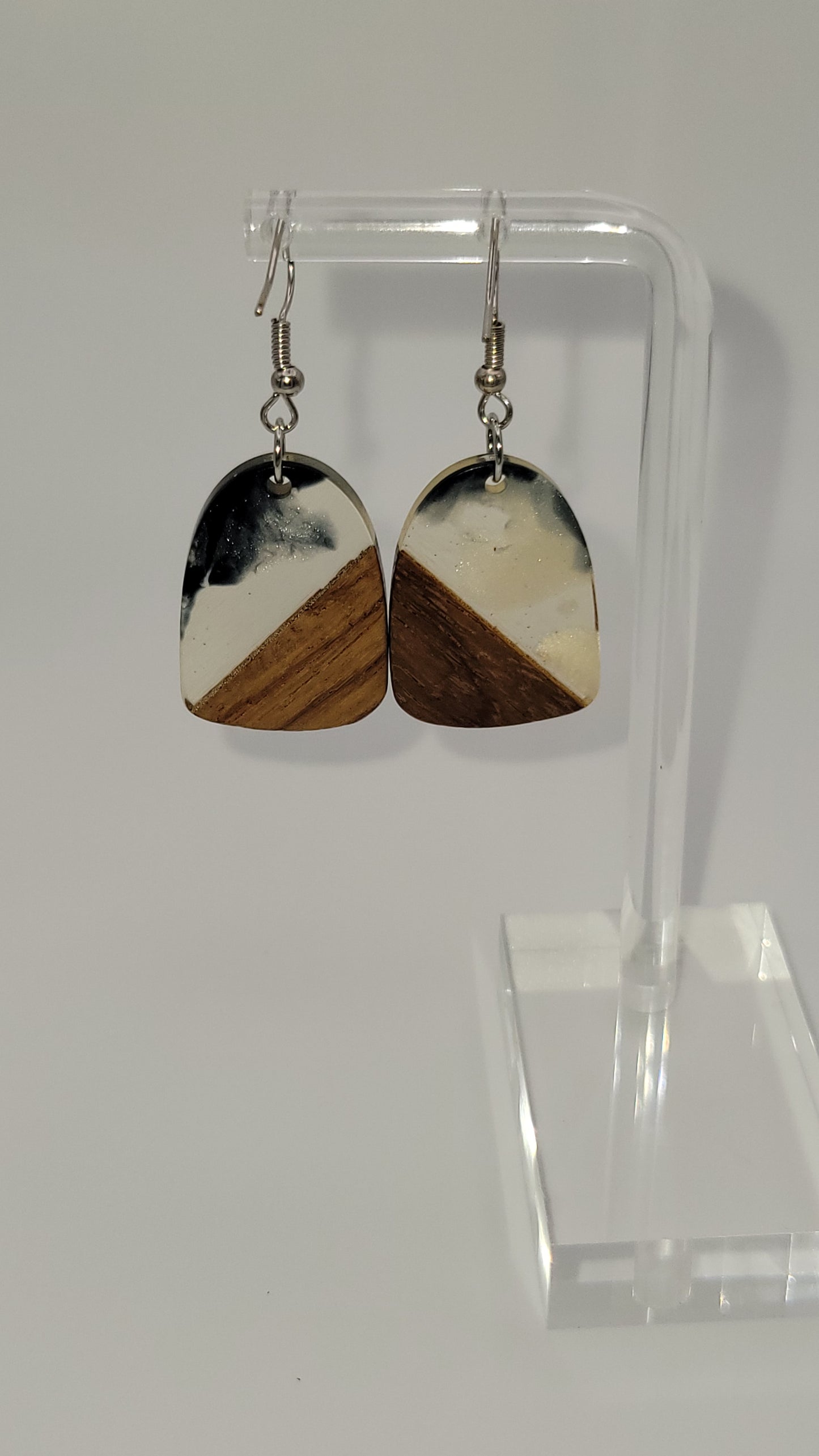 Arch shaped earrings made of wooden and epoxy earring a walnut colored wood.  Colored with a black, white sparkle epoxy. Displayed on a clear stand against a white background