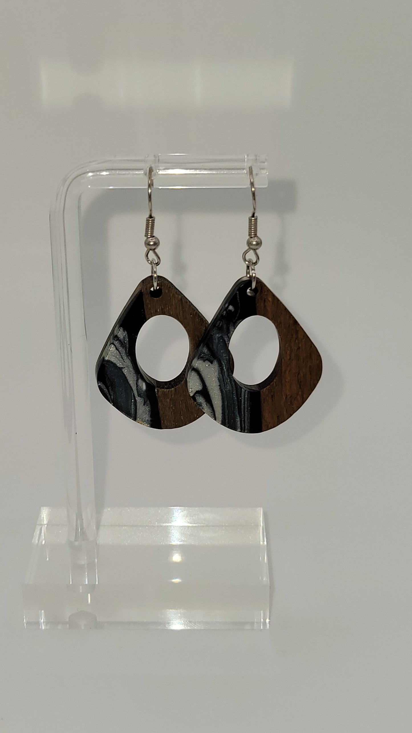 Rounded kite shape earrings made of wooden and epoxy earring a walnut colored wood.  Colored with a black, white sparkle epoxy. Displayed on a clear stand against a white background