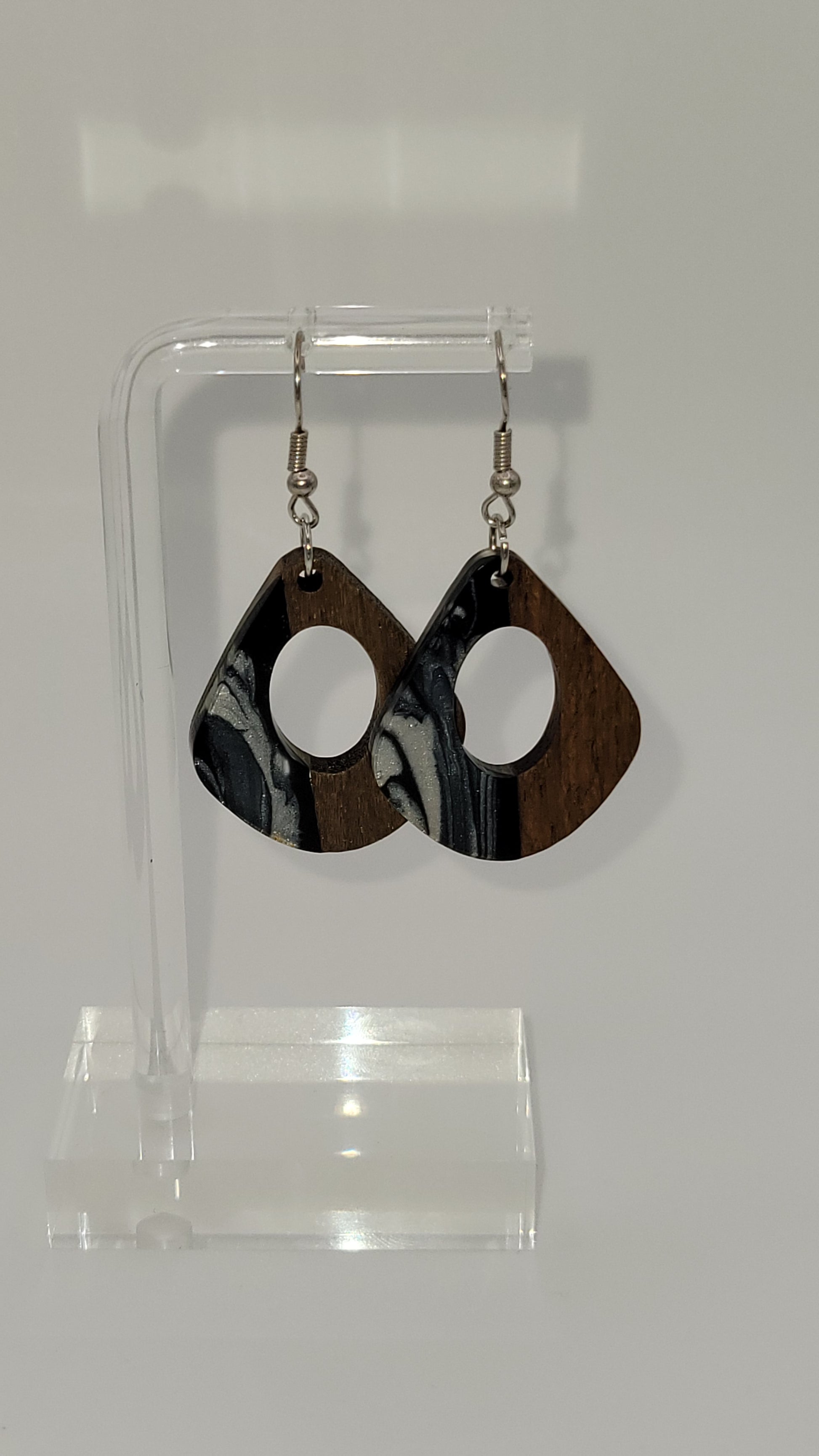 Rounded kite shape earrings made of wooden and epoxy earring a walnut colored wood.  Colored with a black, white sparkle epoxy. Displayed on a clear stand against a white background