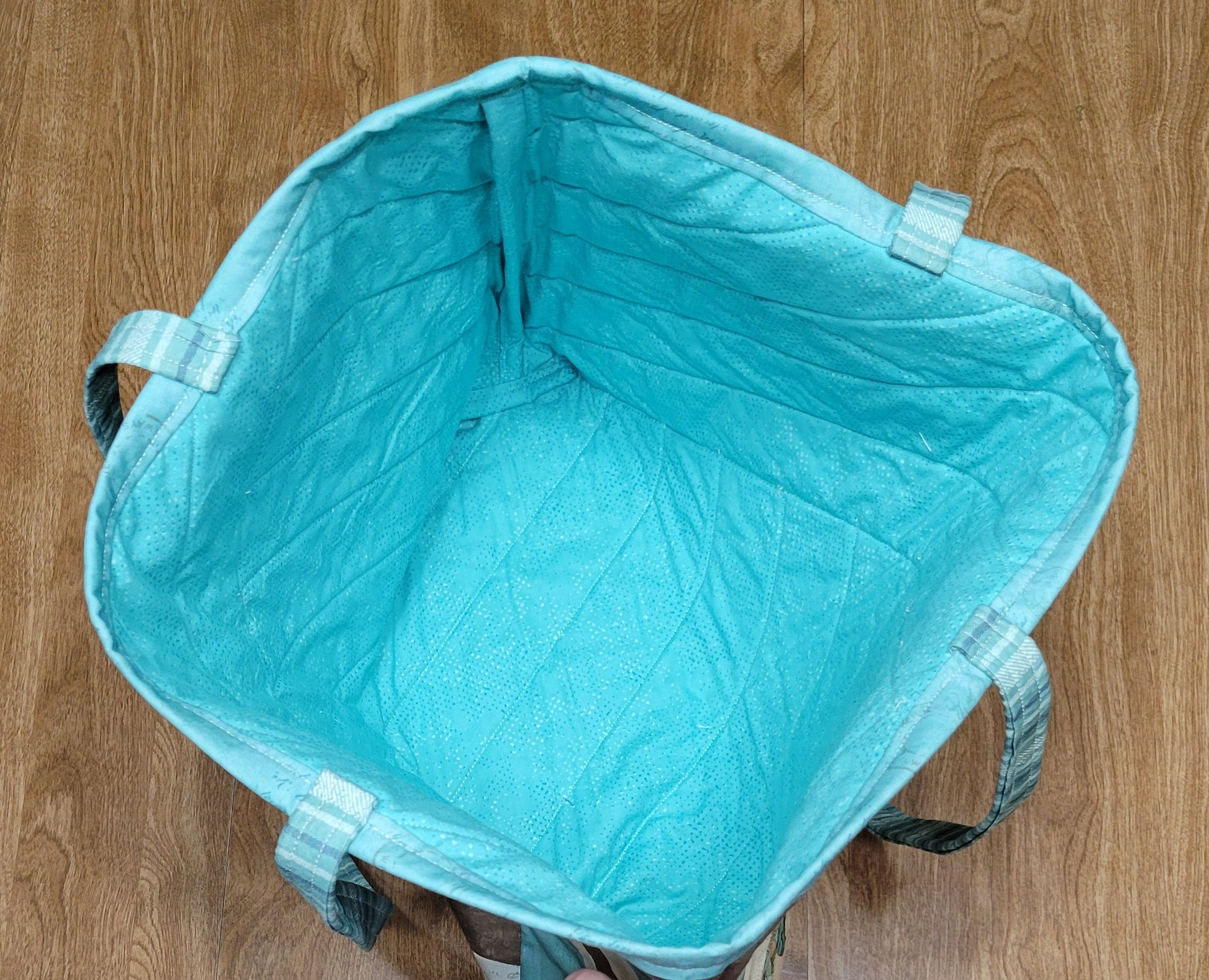 Teal bag on a wooden floor with a person's hand reaching towards it.