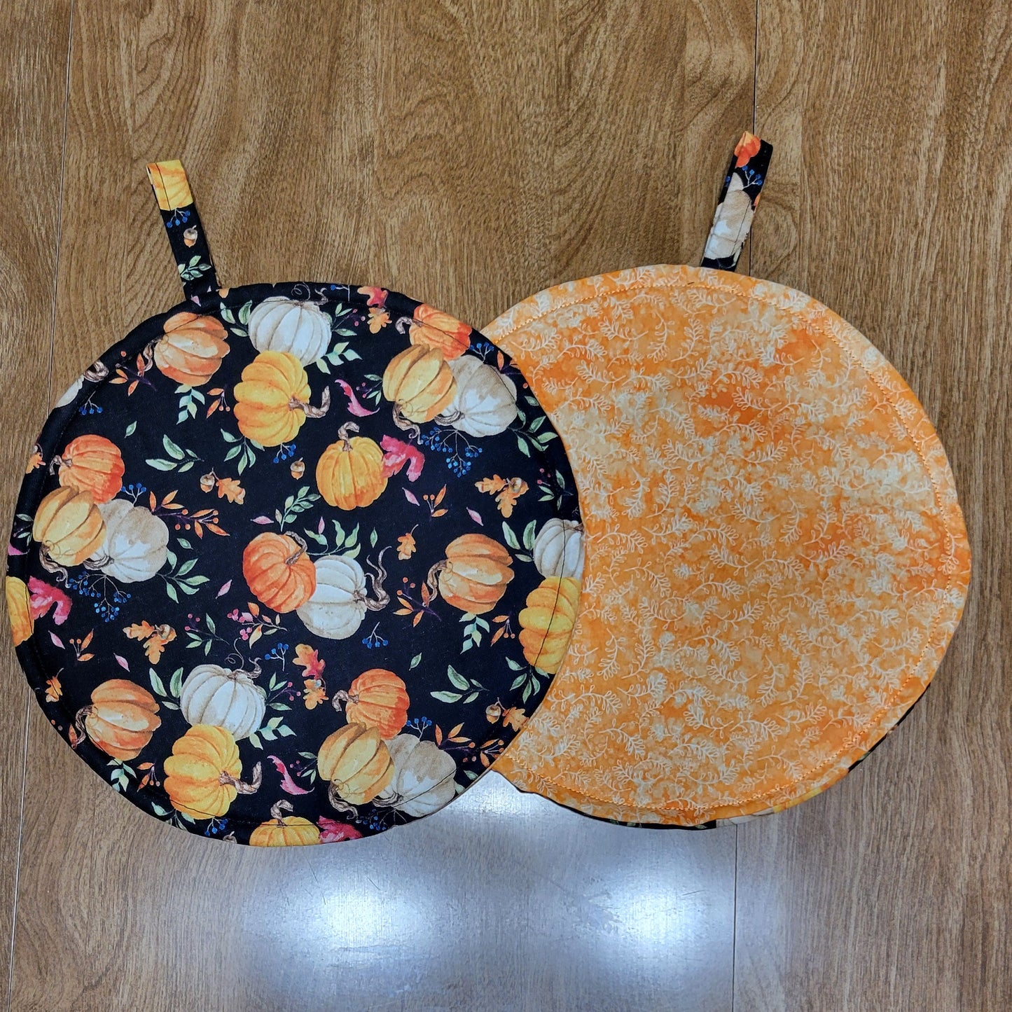 Two round pot holders with pumpkin design on a wooden surface.