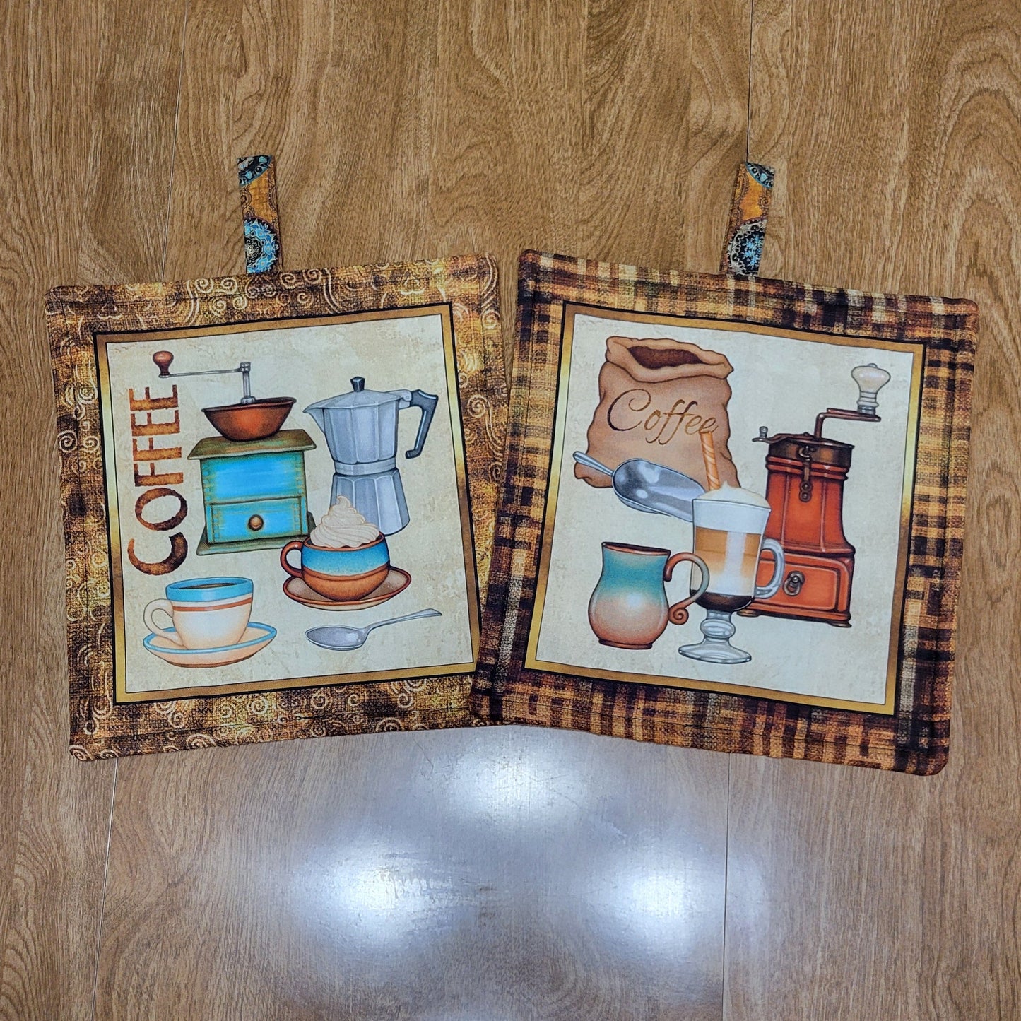 Two coffee-themed pot holders with a brown, black, and golden border on a wood surface