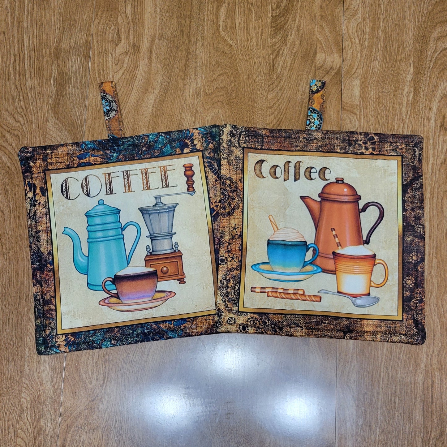Two coffee-themed pot holders with a brown, black, and teal border on a wood surface