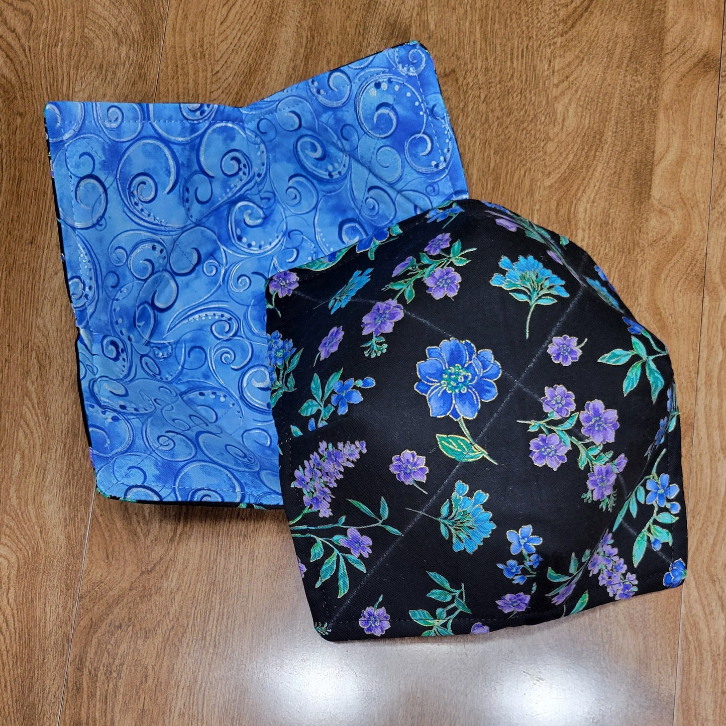 Two fabric samples, one black with floral pattern and one blue with paisley pattern, on a wooden surface.