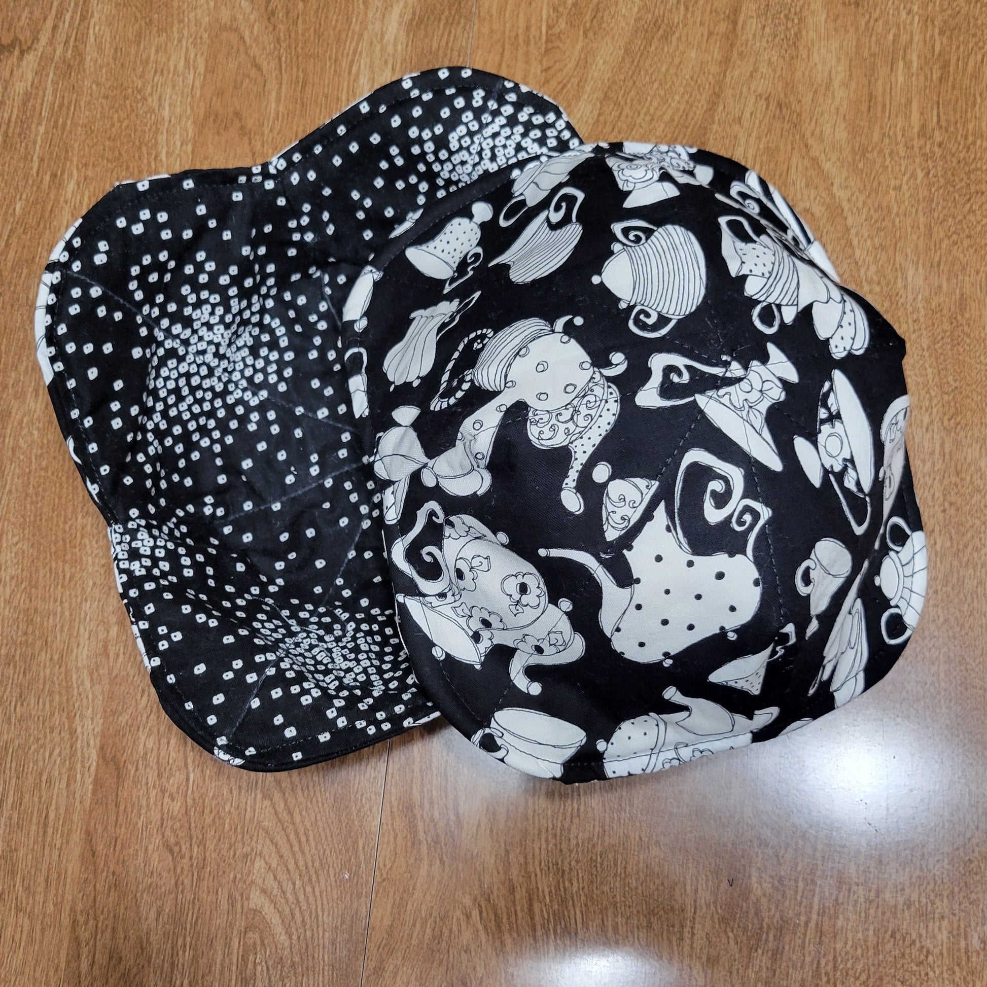Black cozy with white tea pot patterns all over it, on a wooden surface 