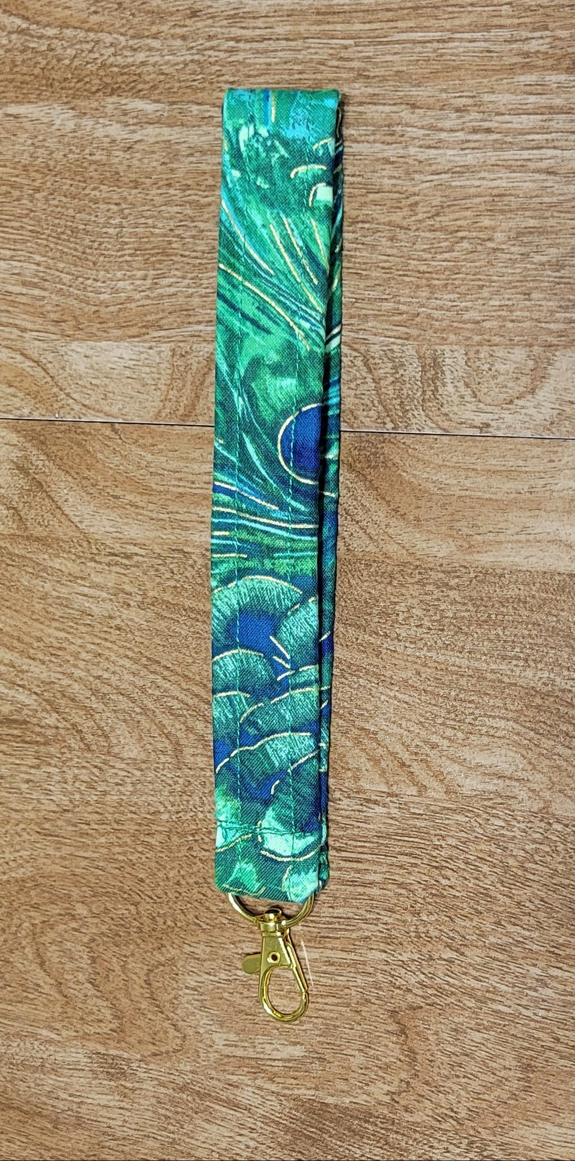 Green peacock feather patterned lanyard on a wooden surface