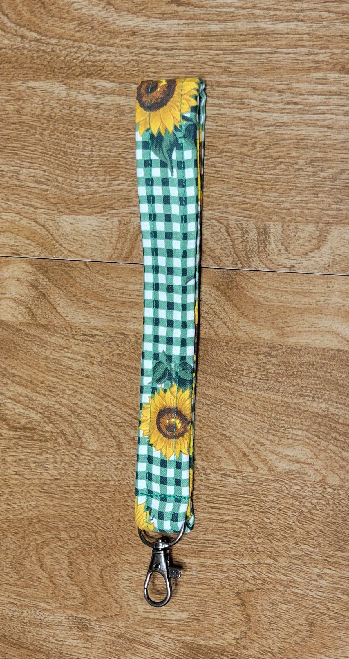 Green checkered lanyard with sunflower design on a wooden surface