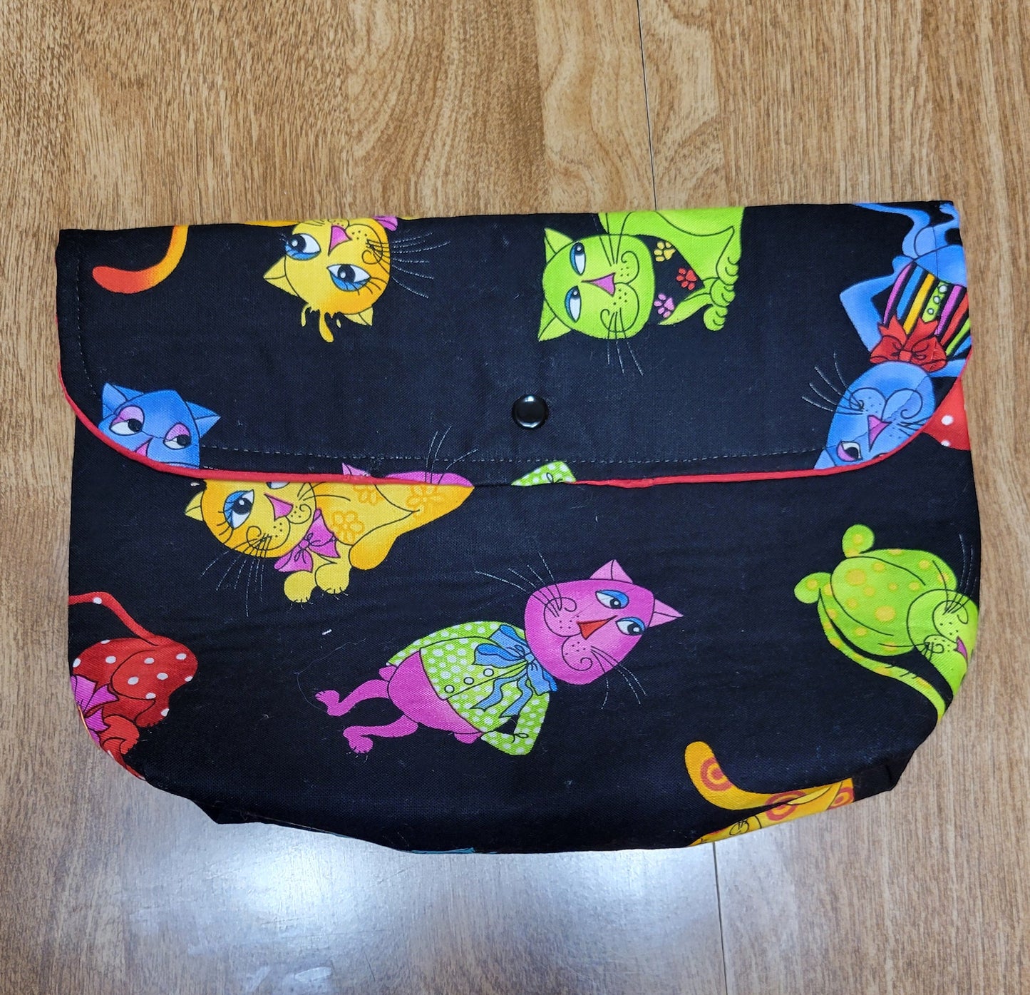 Make up bag with a colorful cats with with a black background, red solid inside with a snap.