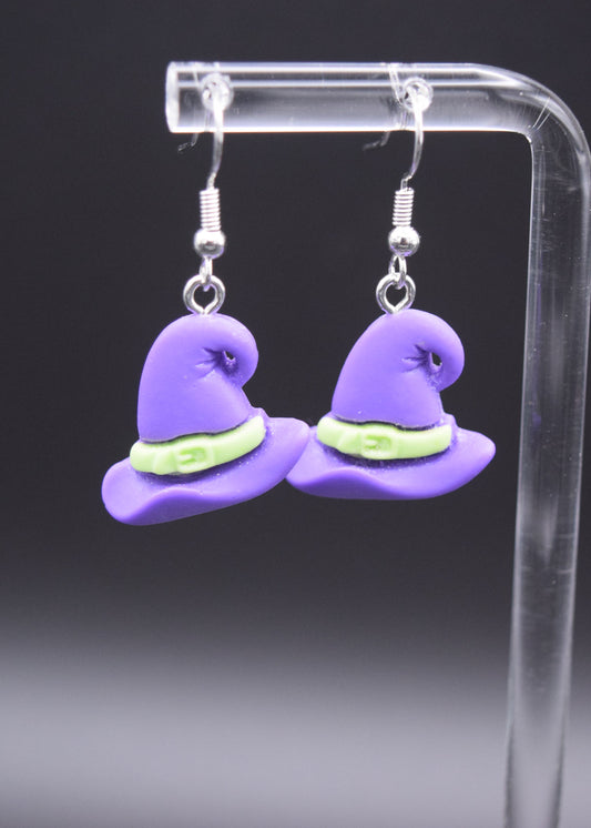 Pair of silicone purple witch with a lime green belt hanging 3/4 inches from a silver hook. Displaying on a clear stand against a black background. 