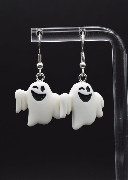 Silicone ghost-shaped earrings with a playful winking expression displayed on a clear stand against a black background