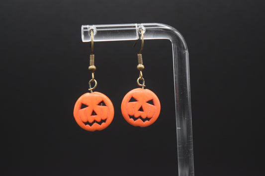 Orange pumpkin-shaped earrings on a clear stand against a black background