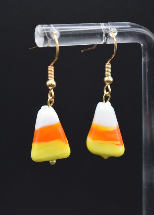 Candy corn-shaped earrings on a clear stand against a black background