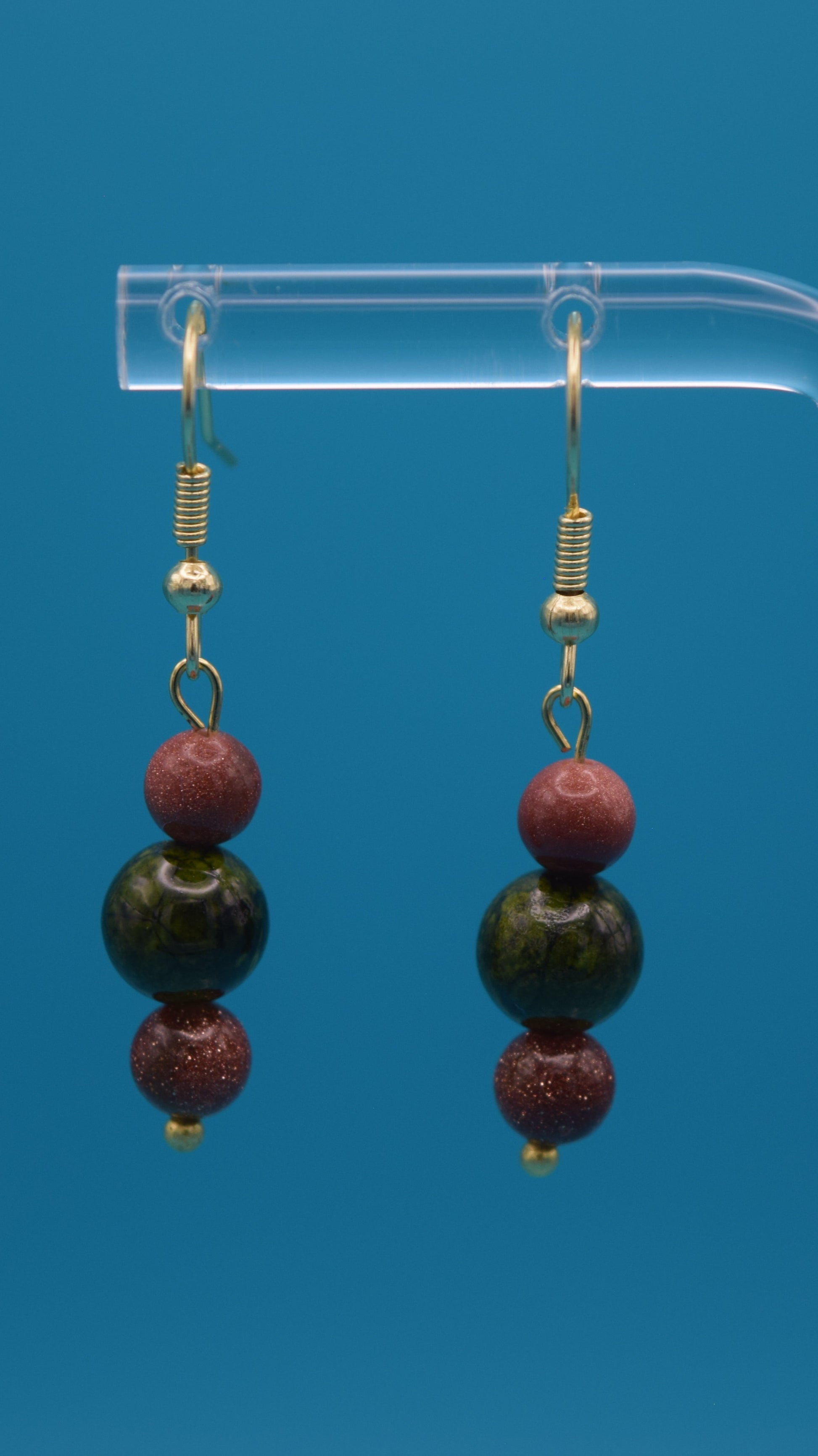 Bronze with gold sparkle on the top and bottom. With a mid-size bead in the center colored with a metallic green bead. Accented with gold. Hanging 3/4 of an inch below the ear.
