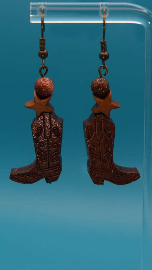 Wooden cowboy boot with a wooden star and a bronze sparkle bead earrings. Displayed on a clear stand against a teal background.