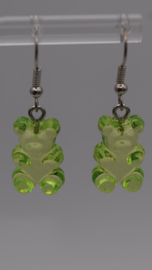Epoxy 2 inch green gummy bear-shaped earrings with silver earring hook. Displayed on a clear stand against a gray background.