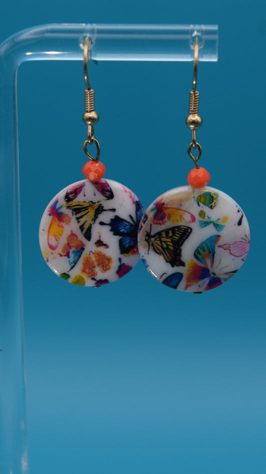 Colorful butterfly-patterned earrings Displayed on a clear stand against a teal background.