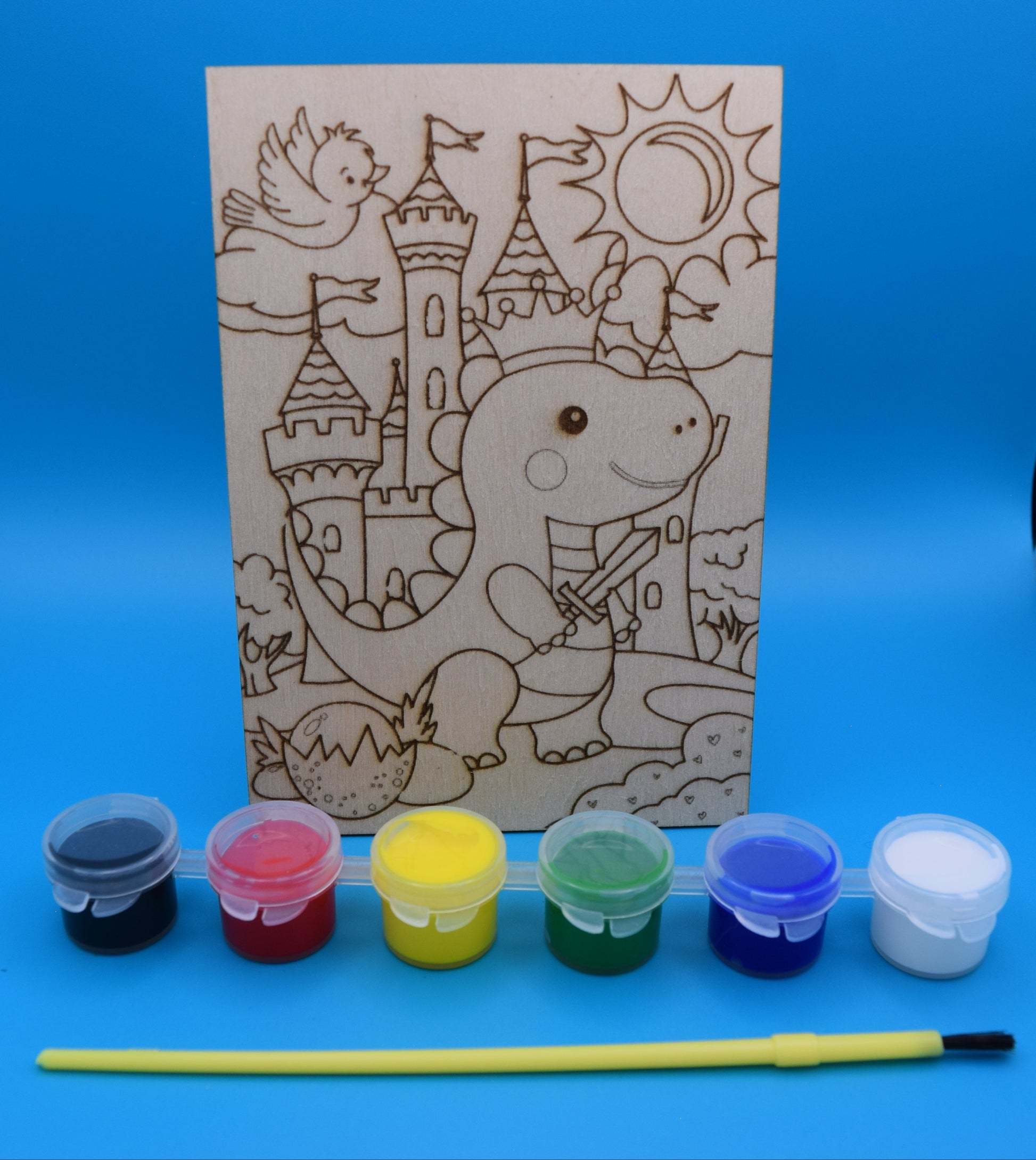 Children's craft kit with a coloring book design of a dinosaur knight a castle and its surroundings, scorn into a 3mm piece of wood, along with paints (black, red, yellow, green, blue and white are provided with a kids paint brush.