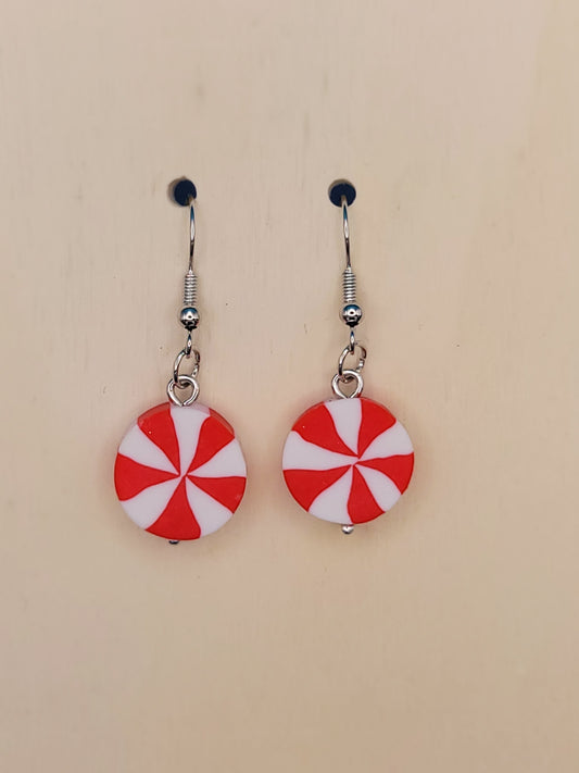 Pair of Silicone red and white peppermint candy dangle earrings. That are 4 cm long with silver hooks and a tiny silver ball on the bottom. Displayed on a beige background.